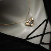 The Golden Orchid pendant by Faceless Jewelry displayed on a mannequin wearing a black lace-up top, featuring a 14Kt gold orchid flower with intricate petal textures on a fine gold chain resting elegantly near the collarbone.