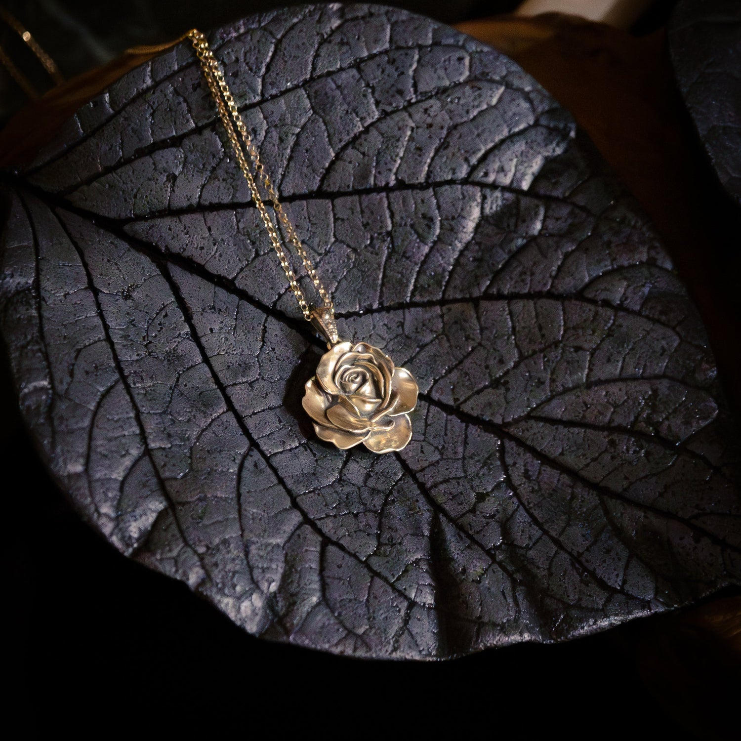 Gold rose necklace on a dark leaf